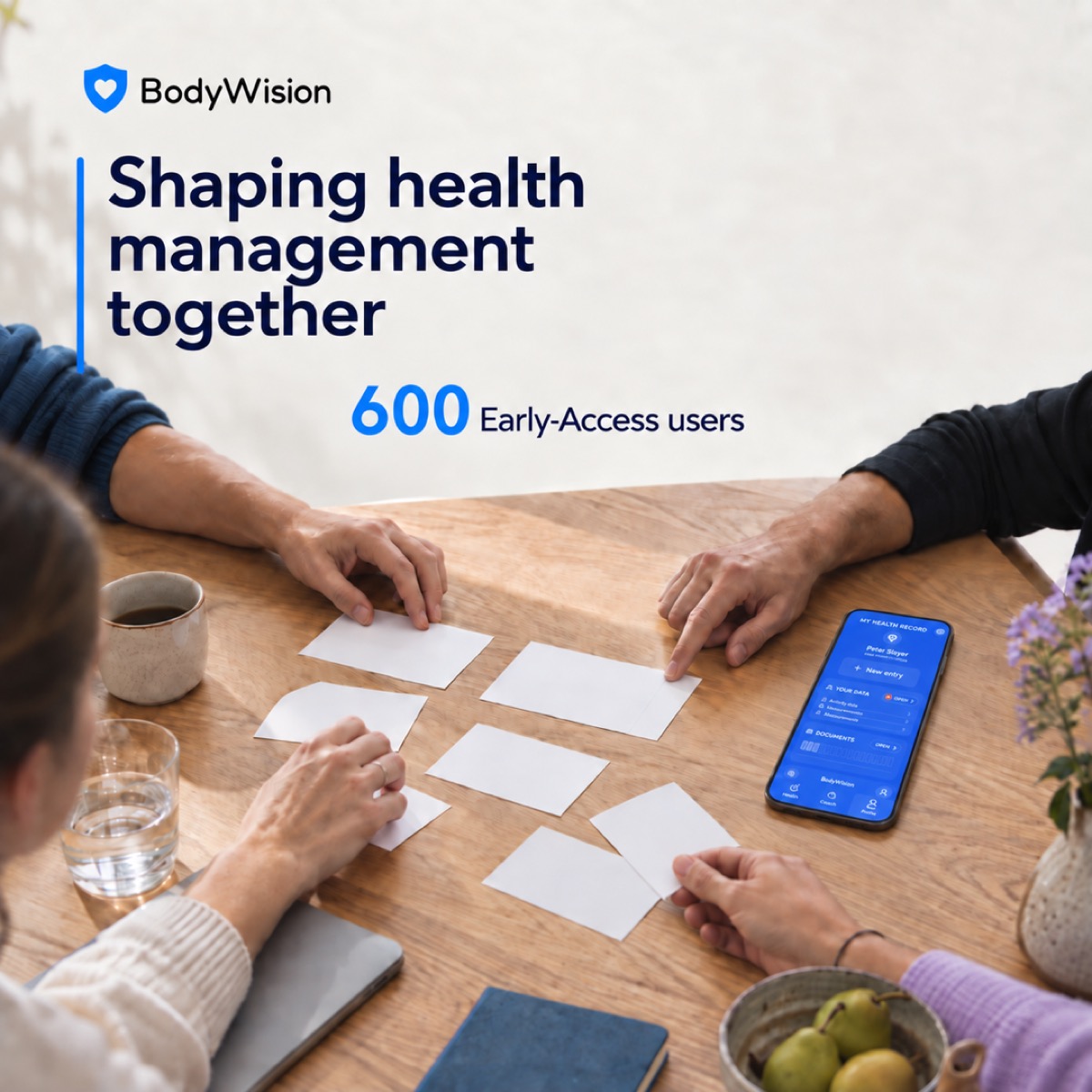 Shaping health management together: 600 Early Access users, a co-design session around a table and the BodyWision health record on a smartphone.